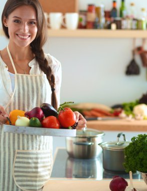 Mutfakta elinde sebzelerle gülümseyen genç bir kadın.