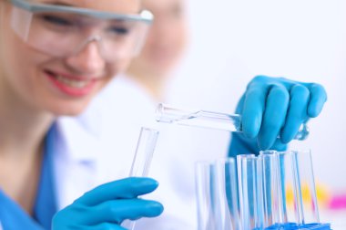 Kadın araştırmacı, beyaz arka planda izole edilmiş ilaç şişeleri ve mataralarla çevrili.