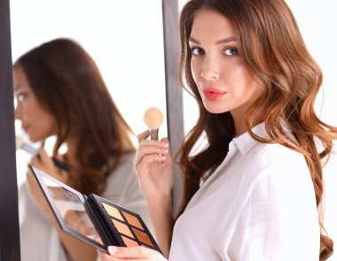 Genç ve güzel bir kadın aynanın yanında makyaj yapıyor.
