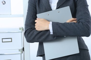 Çekici genç iş kadını masanın yanında elinde dosyayla duruyor.