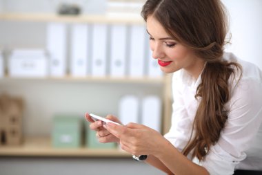 İş kadını ofiste oturan akıllı telefonuyla mesaj gönderiyor.