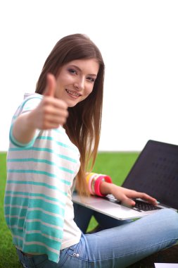 Laptoplu genç bir kadın yeşil çimlerde oturuyor.