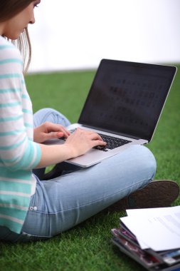Laptoplu genç bir kadın yeşil çimlerde oturuyor.