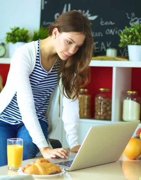 Vonzó fiatal nő használ laptop, és ült a konyhában — Stock Fotó