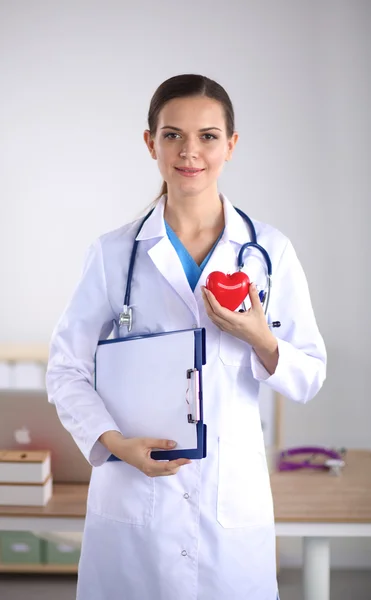 Young woman doctor holding a red heart, standing on gray background — Stock Photo, Image