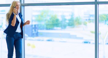 İş kadını ofis penceresinin önünde cep telefonuyla konuşuyor