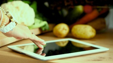 Mutfakta yemek yapmak için tablet bilgisayar kullanan genç bir kadın.
