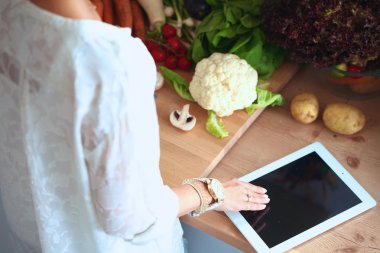 Mutfakta yemek yapmak için tablet bilgisayar kullanan genç bir kadın.
