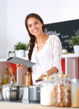 Mutfakta yemek yapmak için tablet bilgisayar kullanan genç bir kadın.