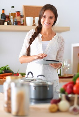 Mutfakta yemek yapmak için tablet bilgisayar kullanan genç bir kadın.