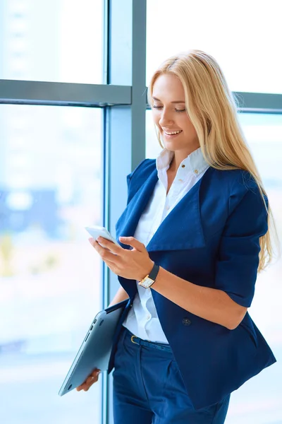 Mujer de negocios de pie contra la ventana de la oficina hablando por teléfono móvil — Foto de Stock