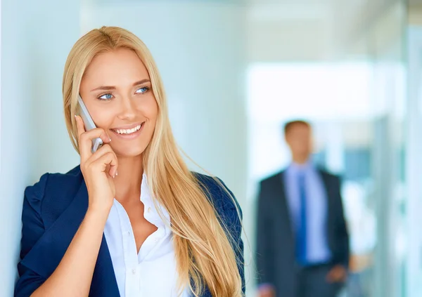 Affärskvinna står mot kontorsfönster talar på mobiltelefon — Stockfoto