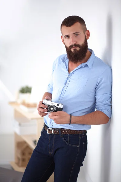 Homem barba jovem segurando uma câmera enquanto de pé contra o fundo branco — Fotografia de Stock