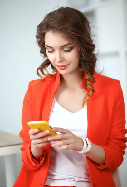 Beautiful businesswoman using cell phone standing in office — Stock Photo, Image