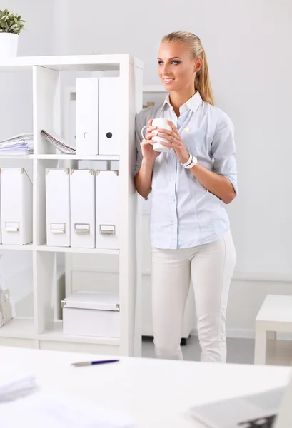 Aantrekkelijke jonge zakenvrouw staat in de buurt van een bureau in het kantoor — Stockfoto