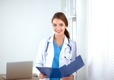 Güzel, genç, gülümseyen bayan doktor masada oturuyor ve yazıyor..