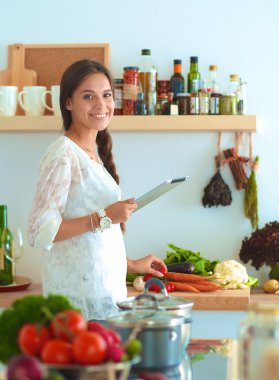 Mutfakta yemek yapmak için tablet bilgisayar kullanan genç bir kadın.