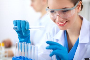 Kadın araştırmacı, beyaz arka planda izole edilmiş ilaç şişeleri ve mataralarla çevrili.