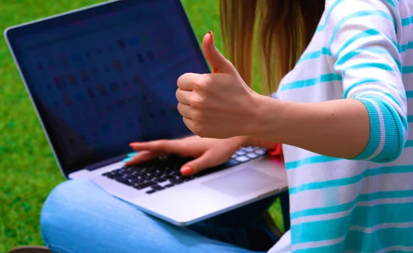 Młoda kobieta z laptopem siedzi na zielonej trawie — Zdjęcie stockowe