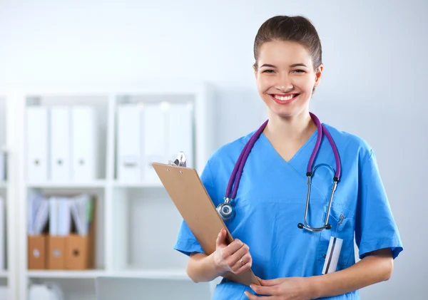 Médico sonriente con una carpeta en uniforme de pie en el hospital — Foto de Stock