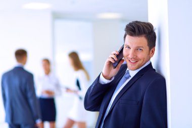 Ofisteki genç iş adamının portresi. Arka planda meslektaşları var ve cep telefonu kullanıyor.