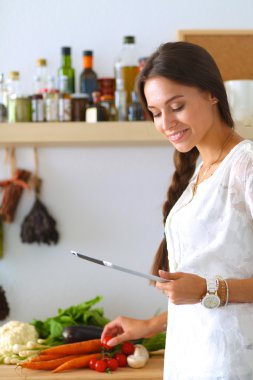 Mutfakta yemek yapmak için tablet bilgisayar kullanan genç bir kadın.