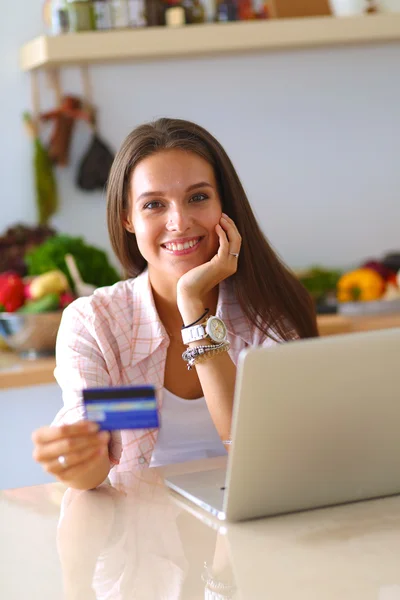 Lachende vrouw online winkelen met behulp van Tablet PC- en creditcard in keuken — Stockfoto