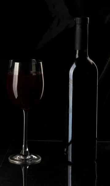 Copo de vinho elegante e uma garrafa de vinho em fundo preto — Fotografia de Stock