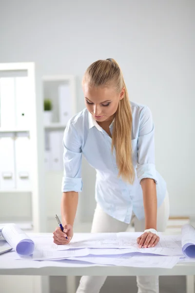 Portrait of female architect with blueprints at desk in office — Stock Photo, Image