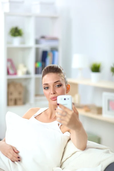 Junge schöne Frau sitzt auf der Couch in ihrem Zimmer mit dem Handy — Stockfoto