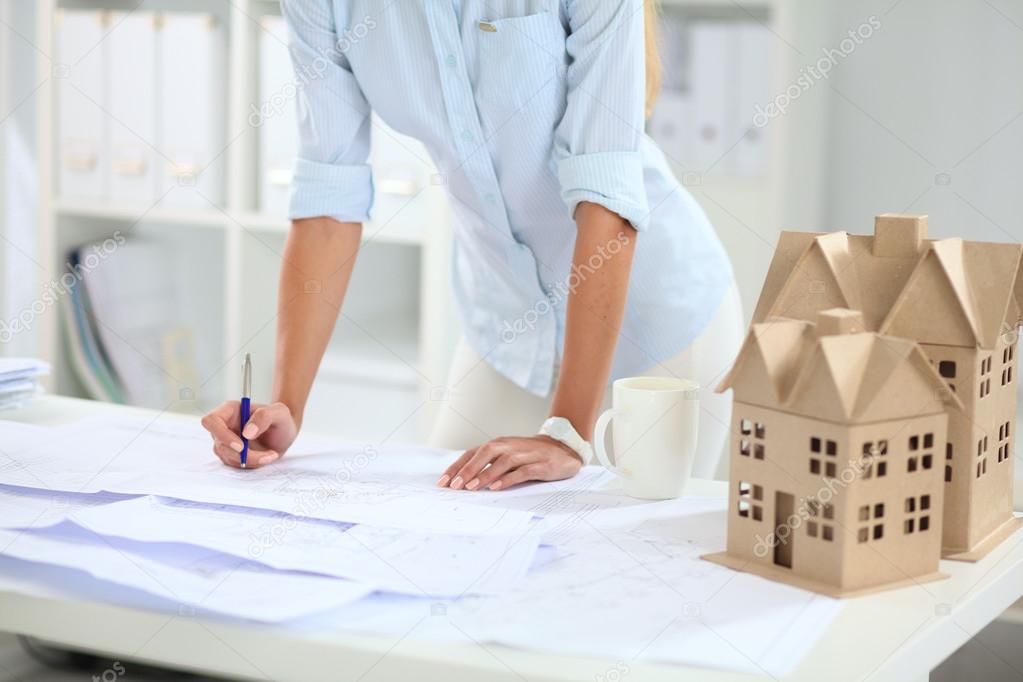 Portrait of female architect with blueprints at desk in office