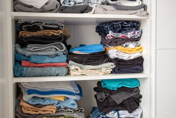 Full messy shelves in white wardrobe with men clothes. Housekeeping concept