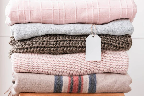 Neatly folded warm clothes in pastel neutral colors with empty white label. Comfortable winter clothes for every day wear