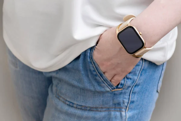Young woman wear blue jeans and white shirt show hand with golden smart watch. Wearable gadget concept.