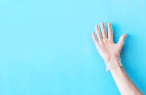 Human hand in transparent vinyl glove raised above light blue background. Safety and selfcare concept. Quality hand protection concept