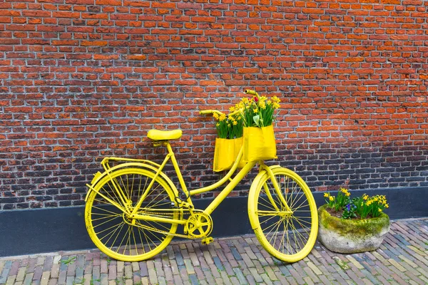 Vibrant yellow bicycle with basket of daffodil flowers on rustic brick wall background