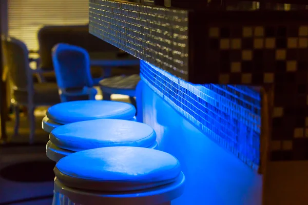 Lege barkrukken langs bar verlichte in blauw licht — Stockfoto