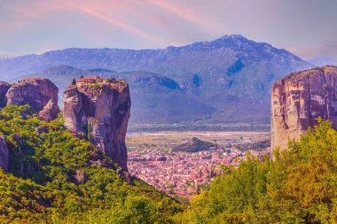 Meteora, Yunanistan, Holy Trinity Manastırı kayalıkların tepesinde ve Kalampaka kasabası vadide, gün batımı manzaralı.