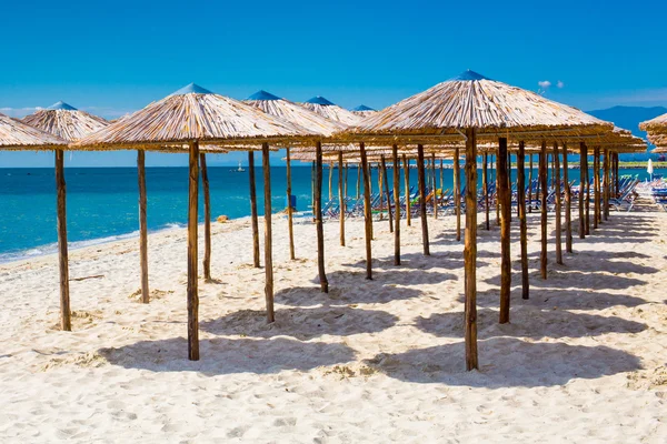 Row of wooden umbrellas at sandy beach, sea and blue sky — Stock Photo, Image