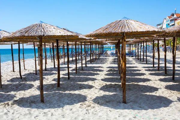 Row of wooden umbrellas at sandy beach, sea and blue sky — Stock Photo, Image