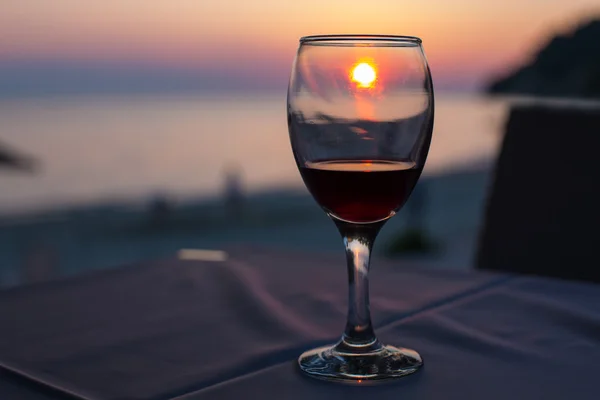 Sunset on beach reflected in glass with red wine , summertime vacation concept