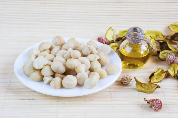 Bodegón con nueces de macadamia en el plato y botella de aceite —  Fotos de Stock