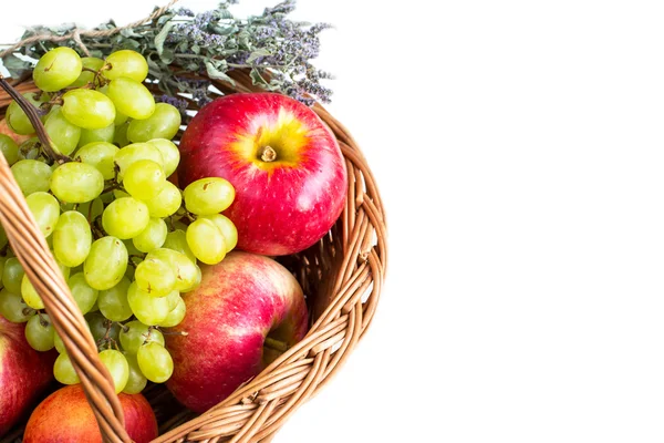 Fondo blanco con manzanas rojas maduras, hierbas de mejorana seca y uvas verdes en la cesta — Foto de Stock