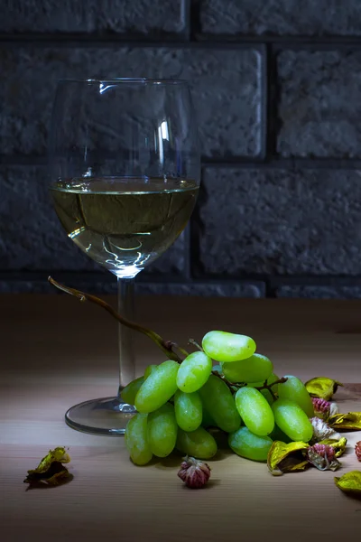 Pohár fehér bor és a szőlő, fából készült asztal és háttér szürke tégla — Stock Fotó
