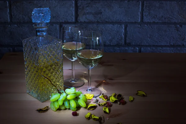 Jarra de cristal de vino blanco, dos copas, uvas sobre mesa de madera y fondo de ladrillos grises —  Fotos de Stock