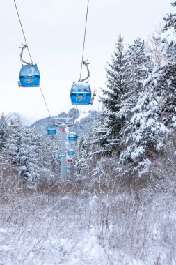 Bansko, Bulgaristan - 21 Ocak 2024: Mavi gondol asansör kulübeleri, kar ormanı çam ağaçları, dağ zirveleri manzaralı kış kayak merkezi manzarası