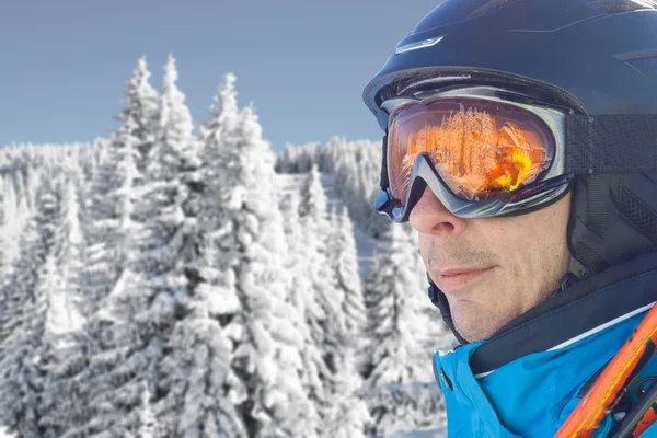 Skier man in the blue skiing jacket, helmet and glasses against snow forest panorama — Stock Photo, Image