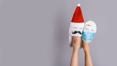 Güzel Noel bacakları. Komik kadın bacakları yüzleri olan terlikler, Noel Baba şapkaları ve koronavirüs yüzünden koruyucu maske takıyor.