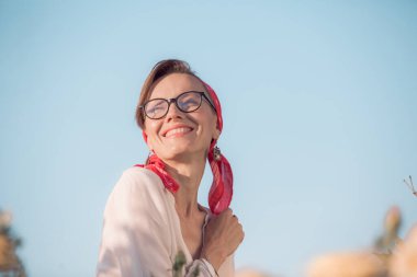 Mutlu genç bir kadın mavi gökyüzünde, yaz güllerinde yürüyor.