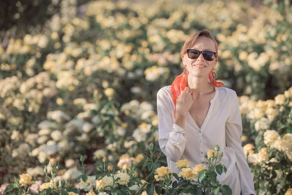 Gün batımında kırsal elbiseli bir kadın, yaz tarlasında gül bahçesinde yürüyor.